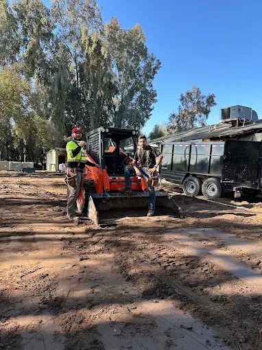 Two Fortify Concrete crew members with a skid steer on a freshly graded lot